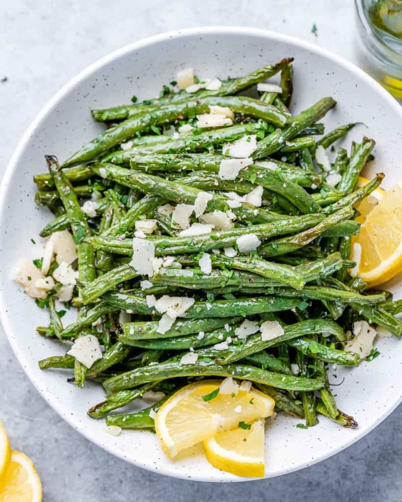 top view cooked green beans topped with shaved parmesan in a round white plate