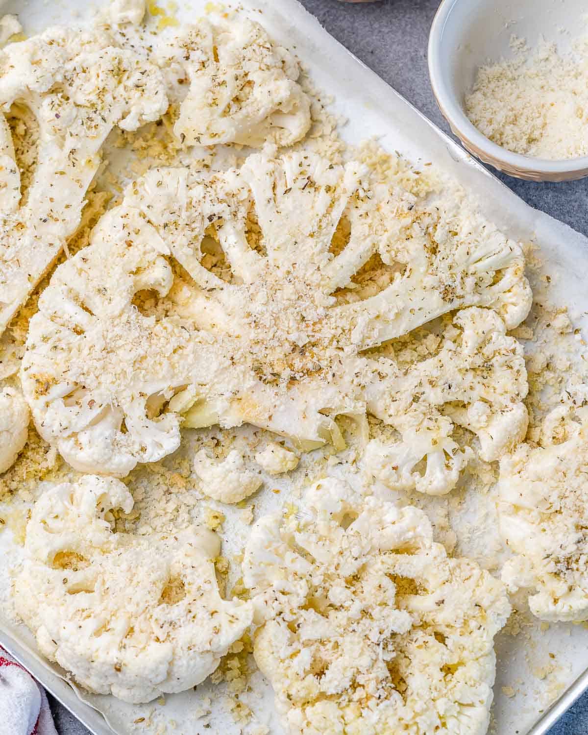cauliflower steaks over a pan topped with parmesan cheese and breadcrumbs before baking