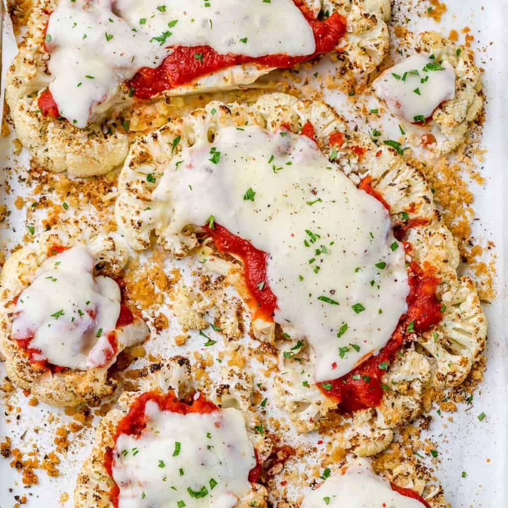 top view of baked cauliflower slices topped with marinara sauce and melted cheese