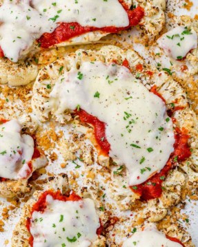 top view of baked cauliflower slices topped with marinara sauce and melted cheese