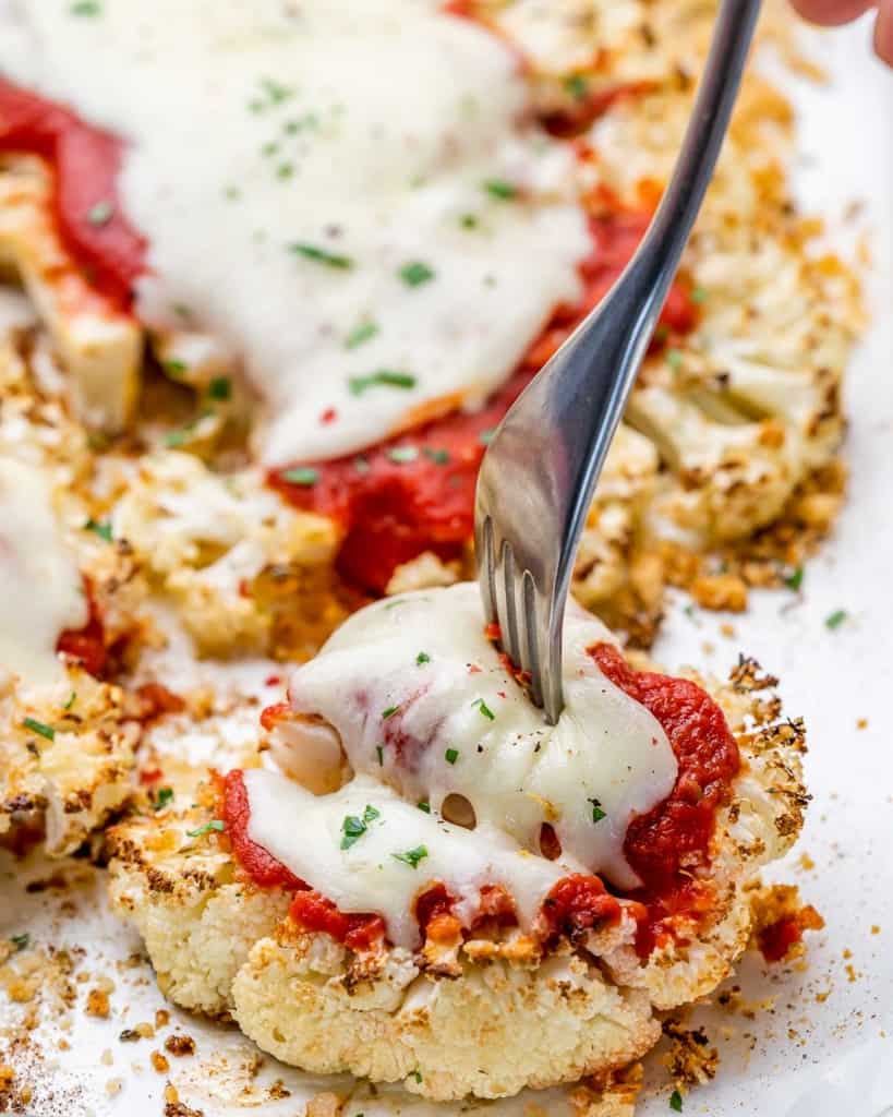 fork on a baked cauliflower steak topped with melted cheese 