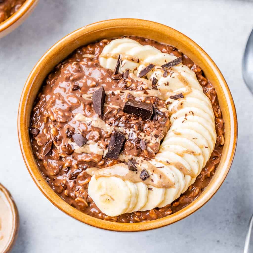 top view chocolate oatmeal topped with sliced bananas and shaved chocolate in a round brown bowl