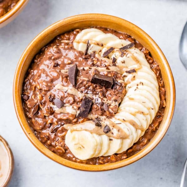 chocolate oatmeal in a brown round bowl topped with sliced bananas and shaved chocolate