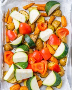 Adding zucchini and bell pepper with potatoes and carrots on a baking pan.