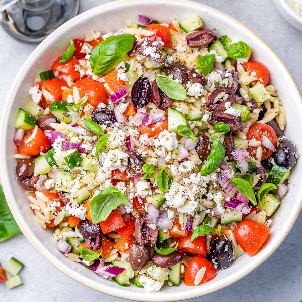 top view orzo salad with a variety of veggie in a round white bowl