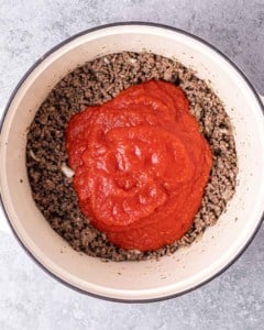 Adding marinara sauce to ground beef in a large pot.