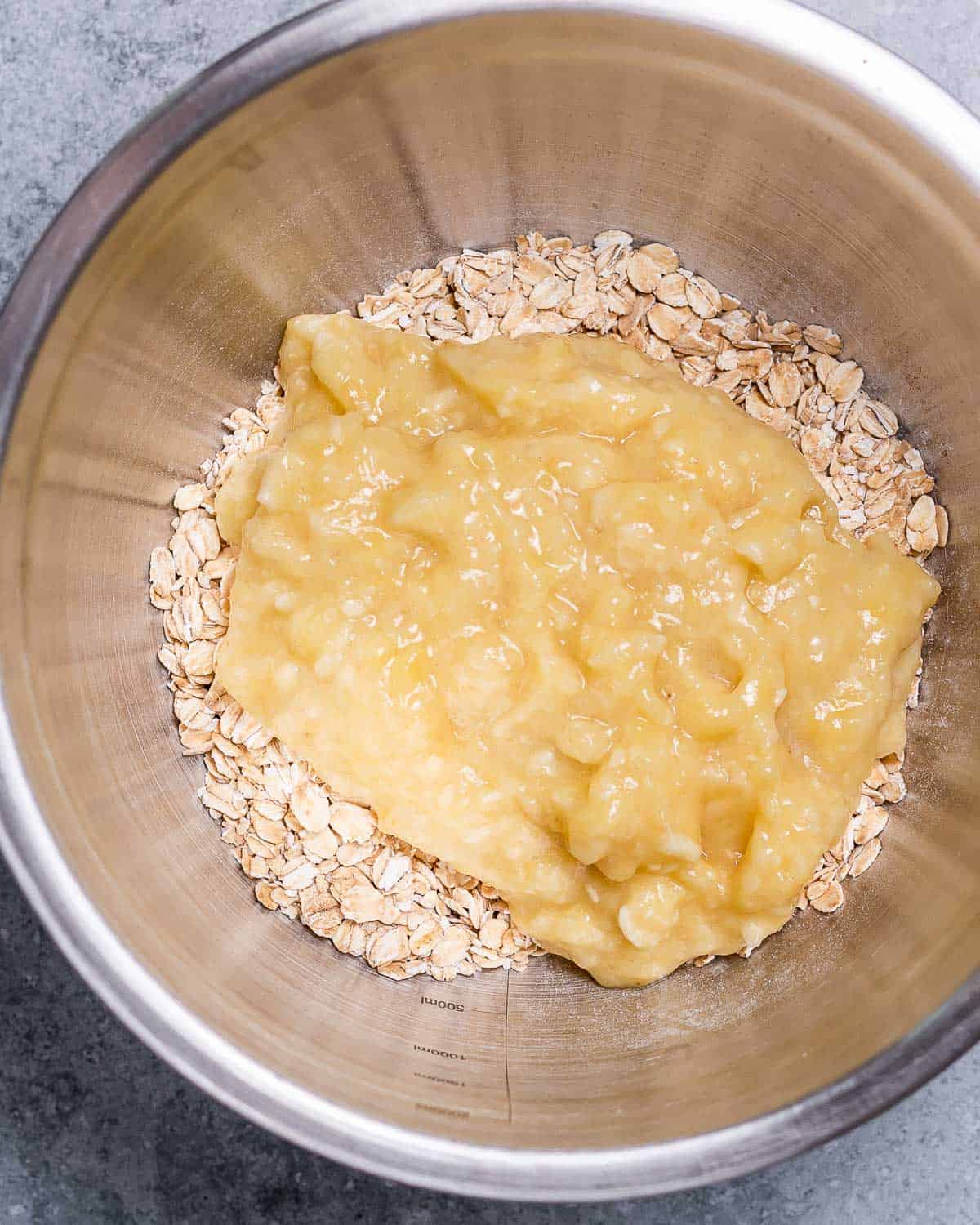 Adding mashed bananas to oats in a large bowl.