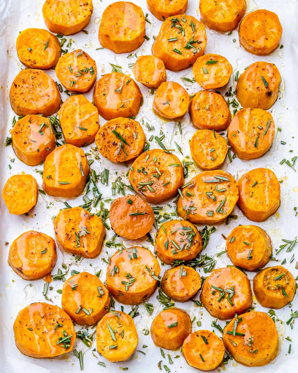 Sweet potato rounds drizzled with honey and garnished with rosemary on a pan.