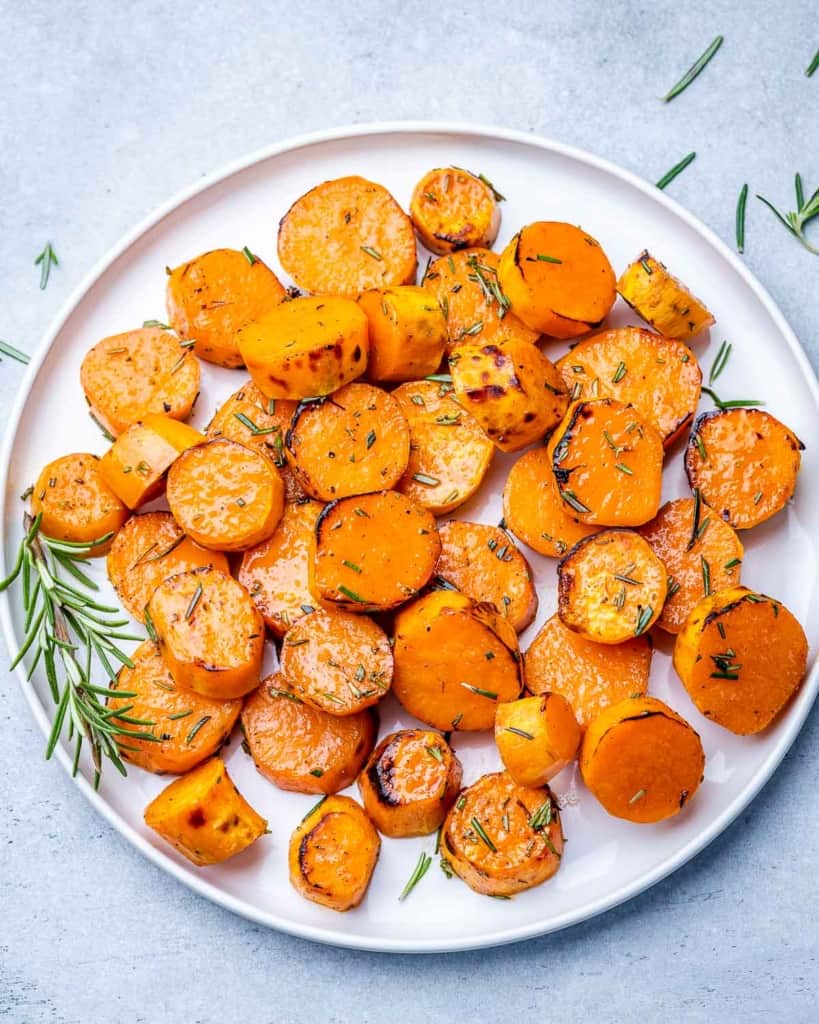 Roasted sweet potatoes on a white plate garnished with a sprig of rosemary.