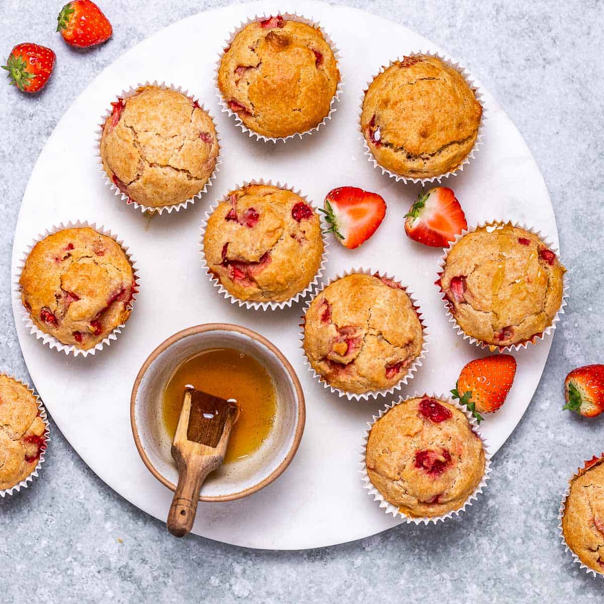 top view of strawberry muffins on a white plate with a small bowl of honey on the side