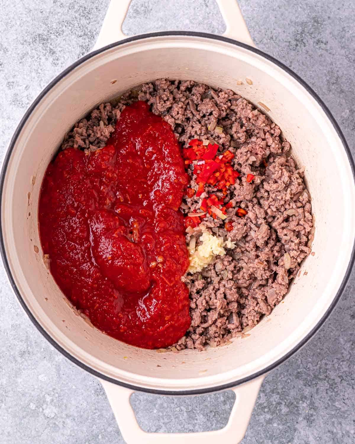 Adding enchilada sauce to ground beef in a pot.
