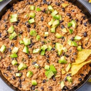 top view chili dip in a skillet topped with green onions and avocado