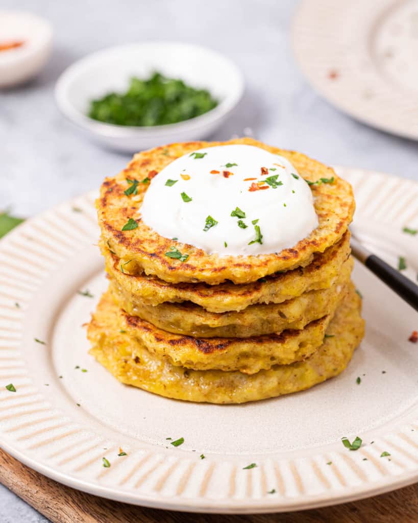 side shot of potato pancakes stacked on each other on a white plate, topped with yogurt