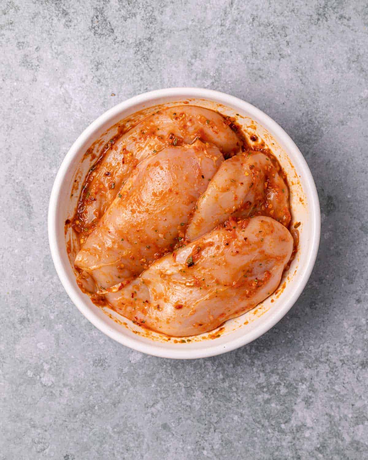Chicken marinating in a white bowl.