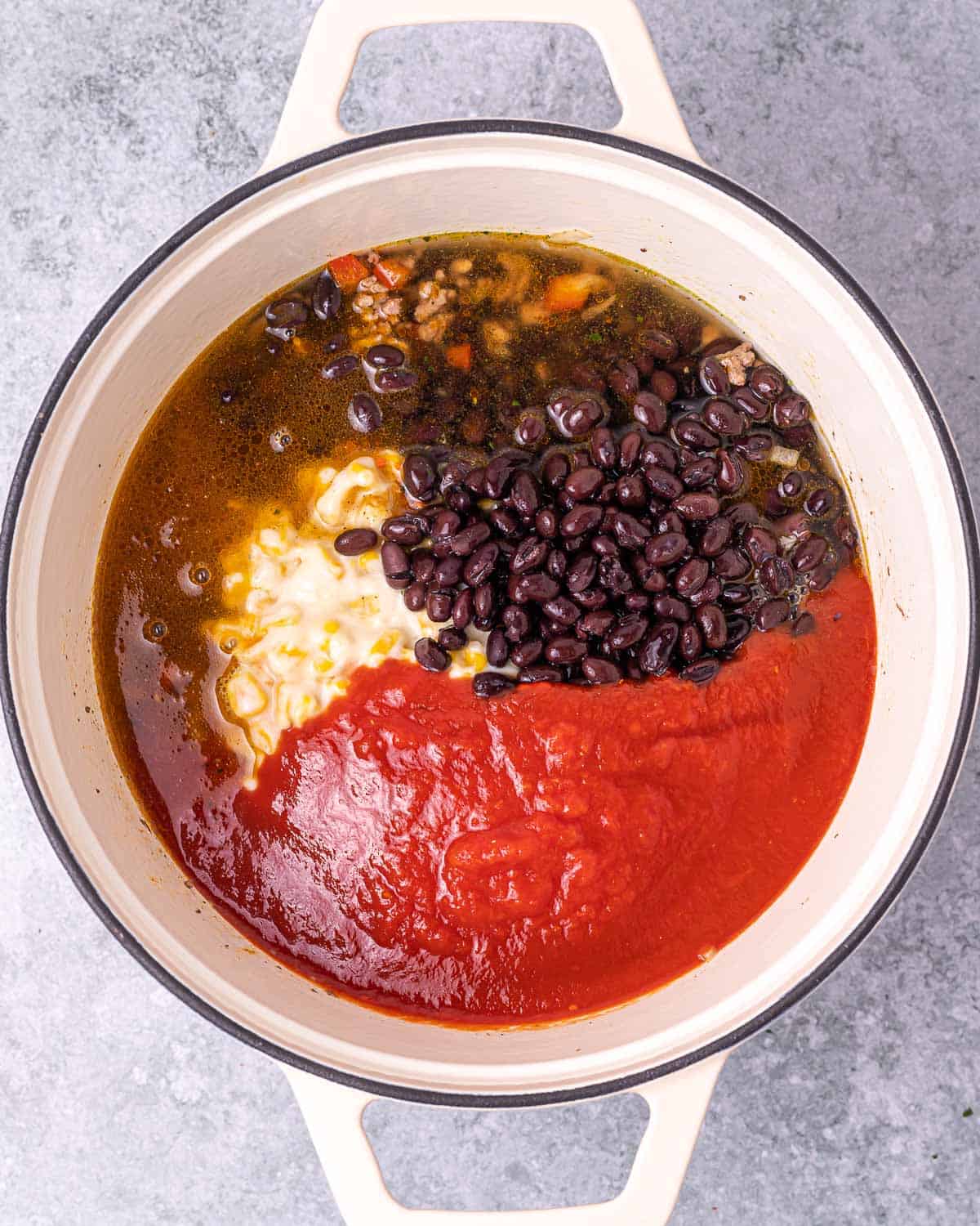 Adding enchilada sauce and black beans to soup pot.