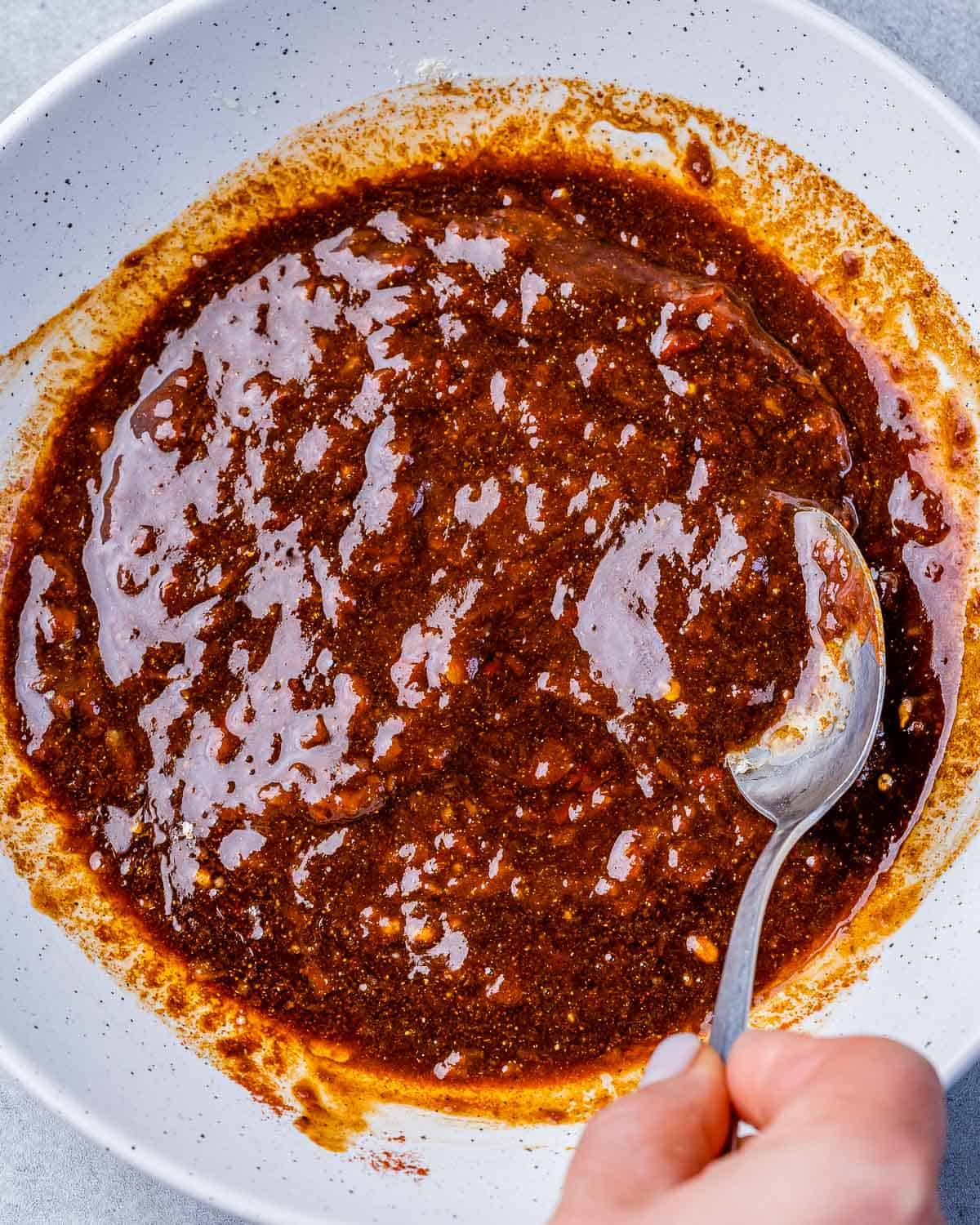 marinade mixed with hand holding spoon in a white bowl