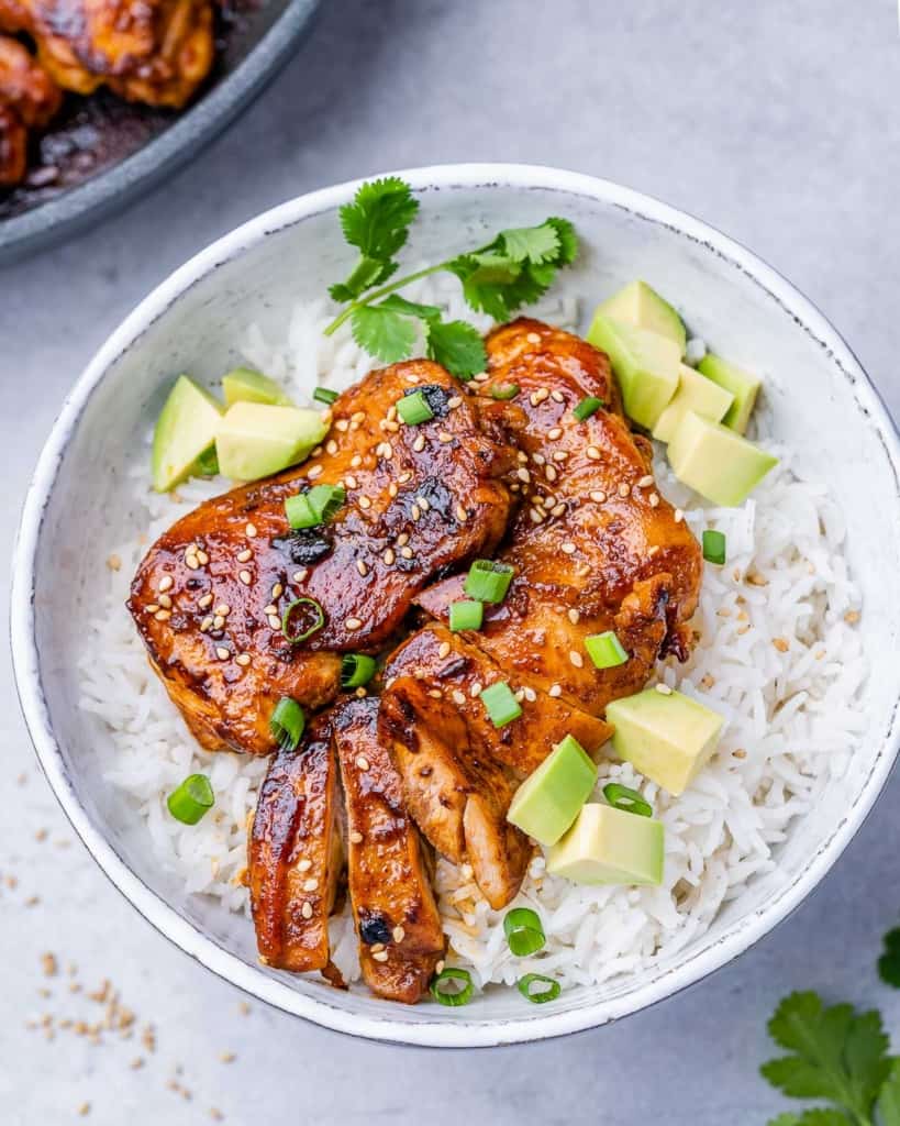 top view chicken thighs over a bowl of white rice topped with green onions and avocado
