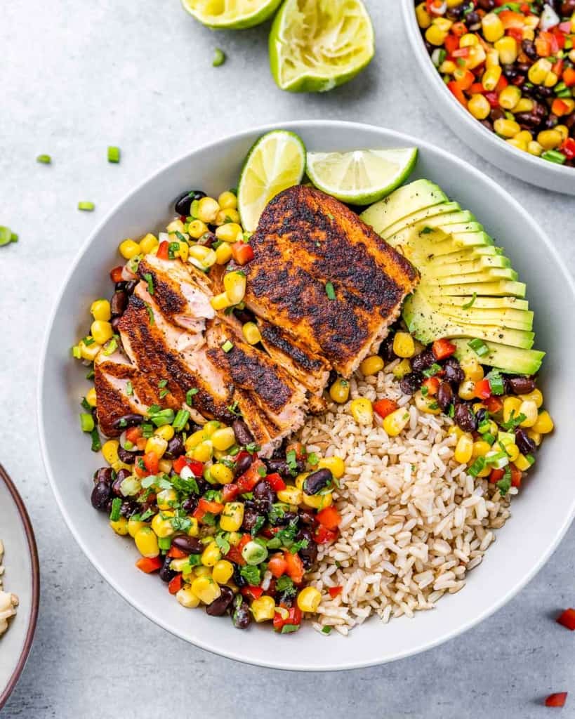 Salmon served in a bowl with brown rice, veggies and avocado. 