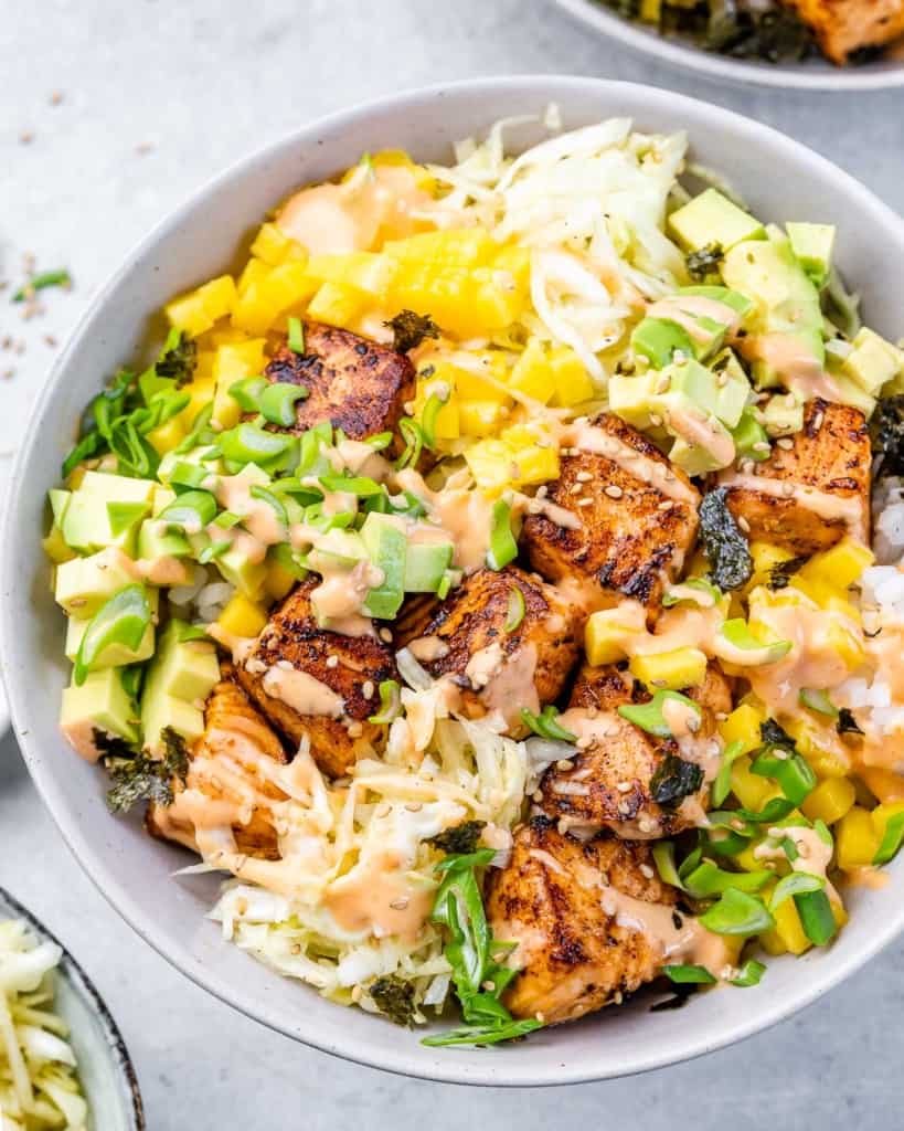 Assembling salmon bowls with rice, cabbage, mango and avocado.