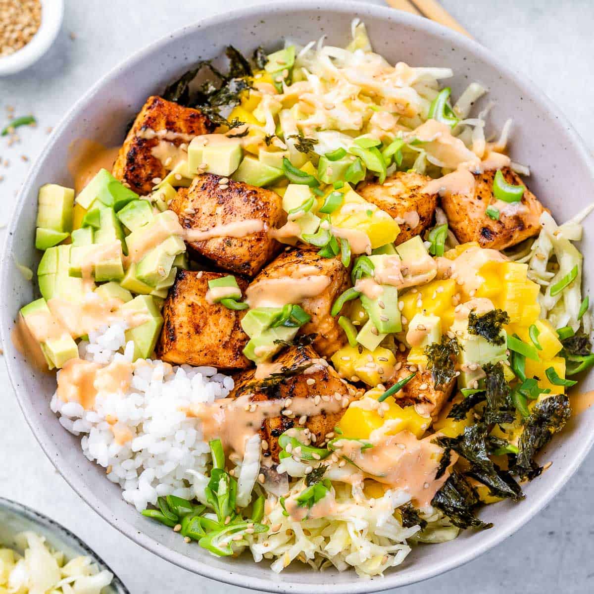 Top view bowl with spicy salmon bites, rice, sauce, avocado, and mango.