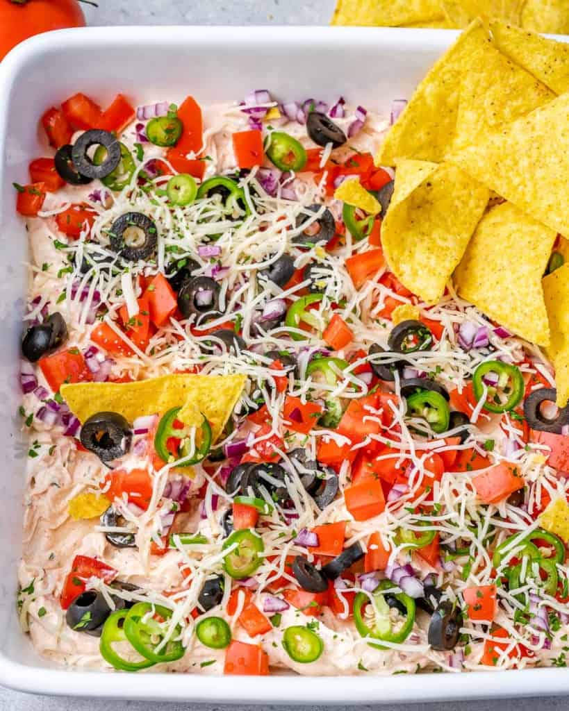 Taco dip in a white serving bowl with corn chips.
