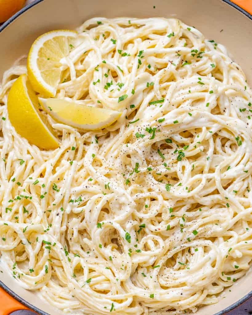 close up image of pasta in a skillet with lemon wedges 