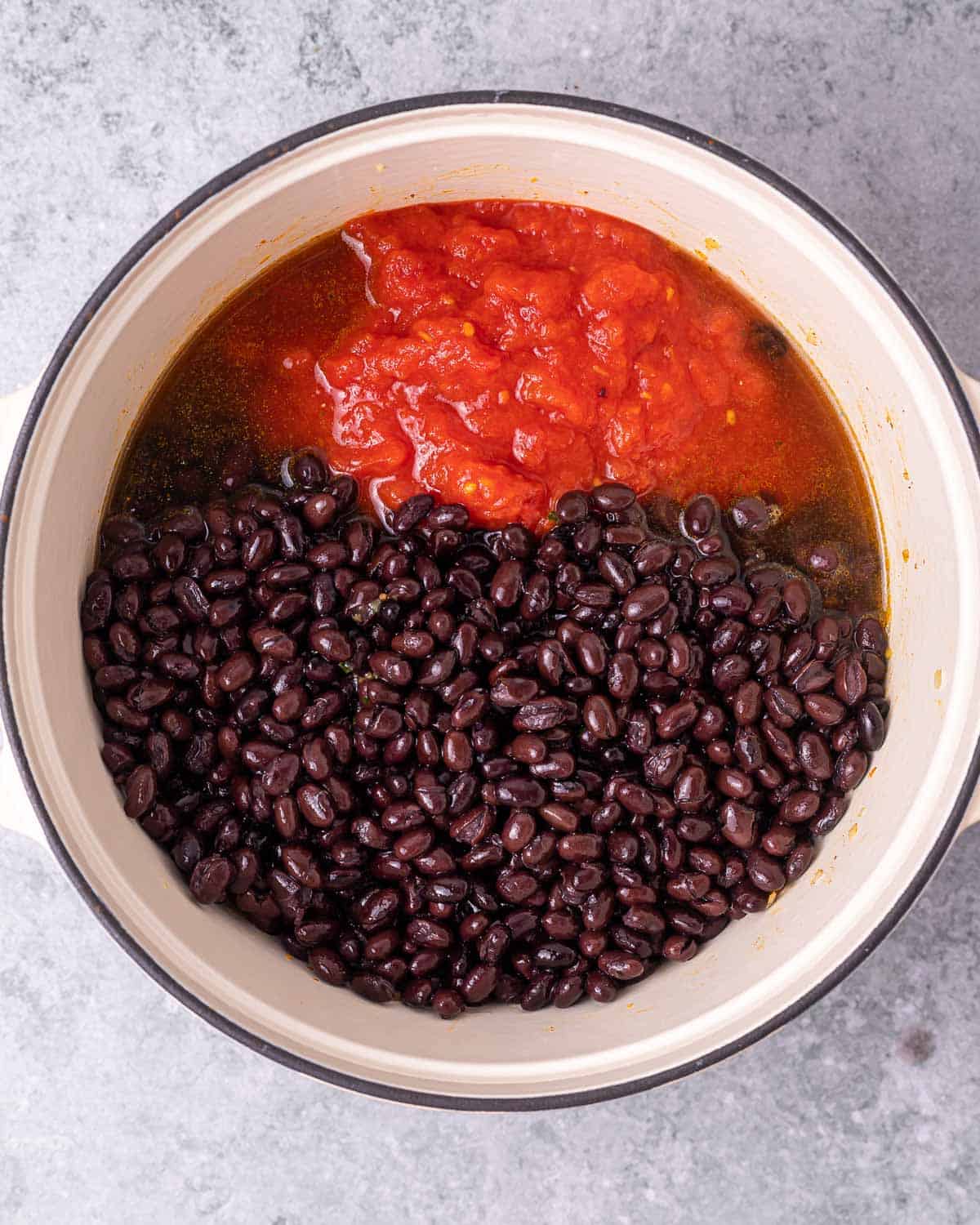 Adding black beans and tomatoes to pot.