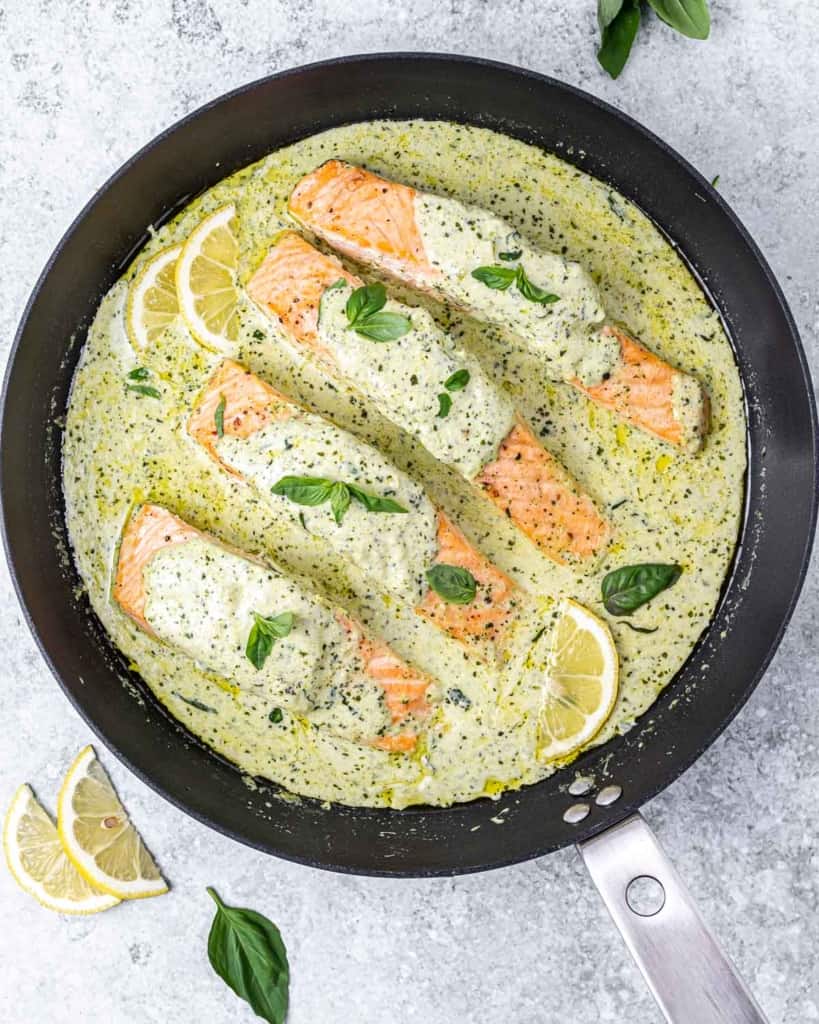 Creamy pesto salmon topped with fresh basil and served with lemon wedges.