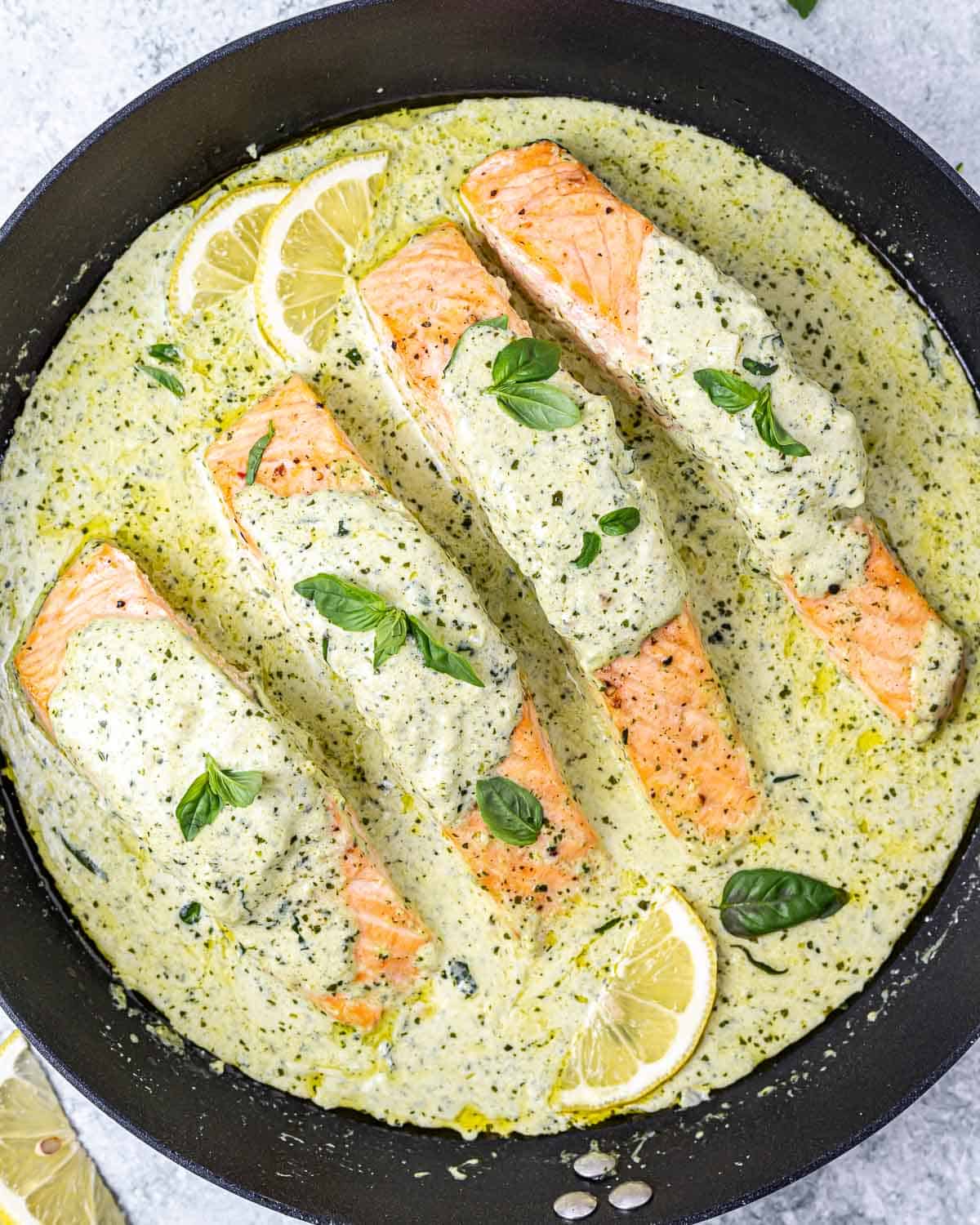top view salmon in a creamy pesto sauce in a black skillet