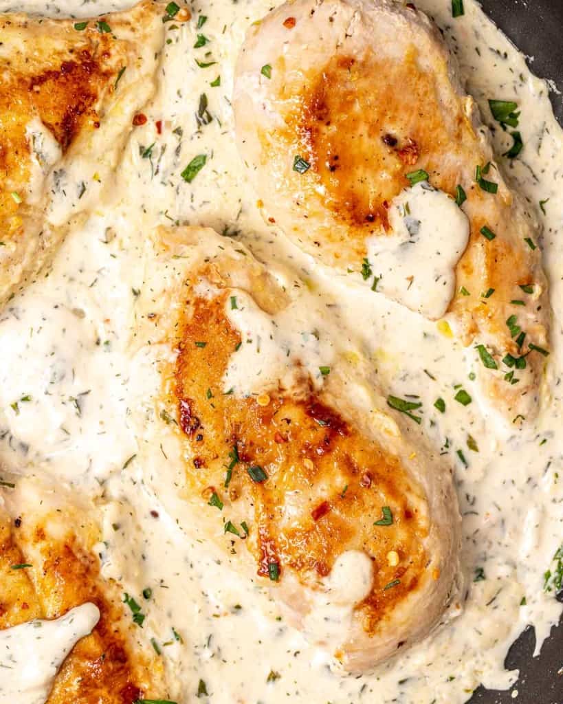 Chicken breasts cooking in a creamy sauce in a skillet.