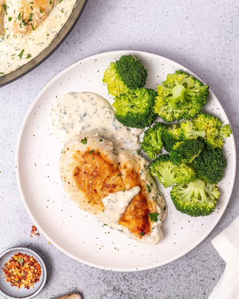 Creamy ranch chicken on a white plate with broccoli.