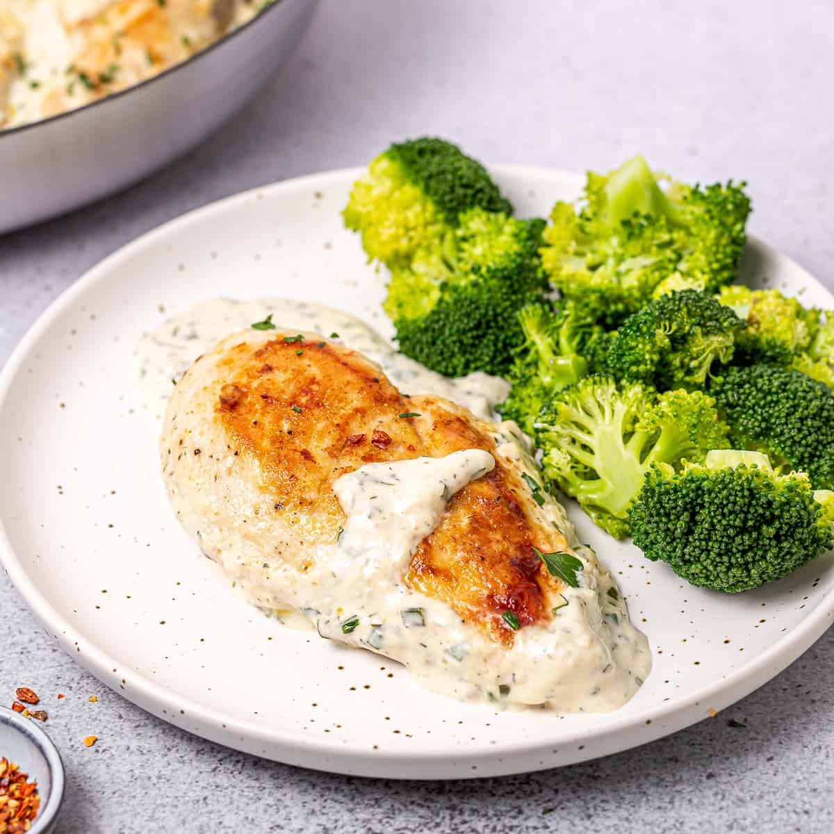 side shot of chicken breast in a creamy ranch sauce with sauteed broccoli side