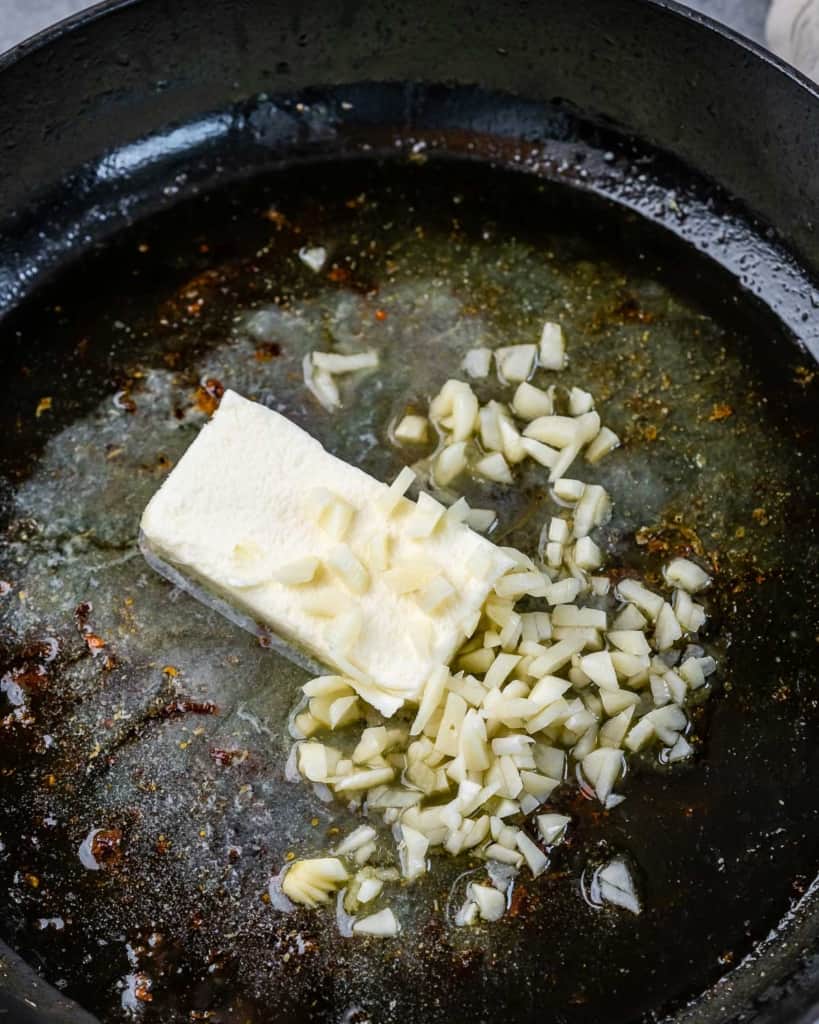 Adding broth, butter and garlic to a pan.