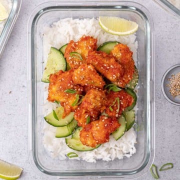 top view honey chicken over white rice and cucumber salad in a glass meal prep bowl