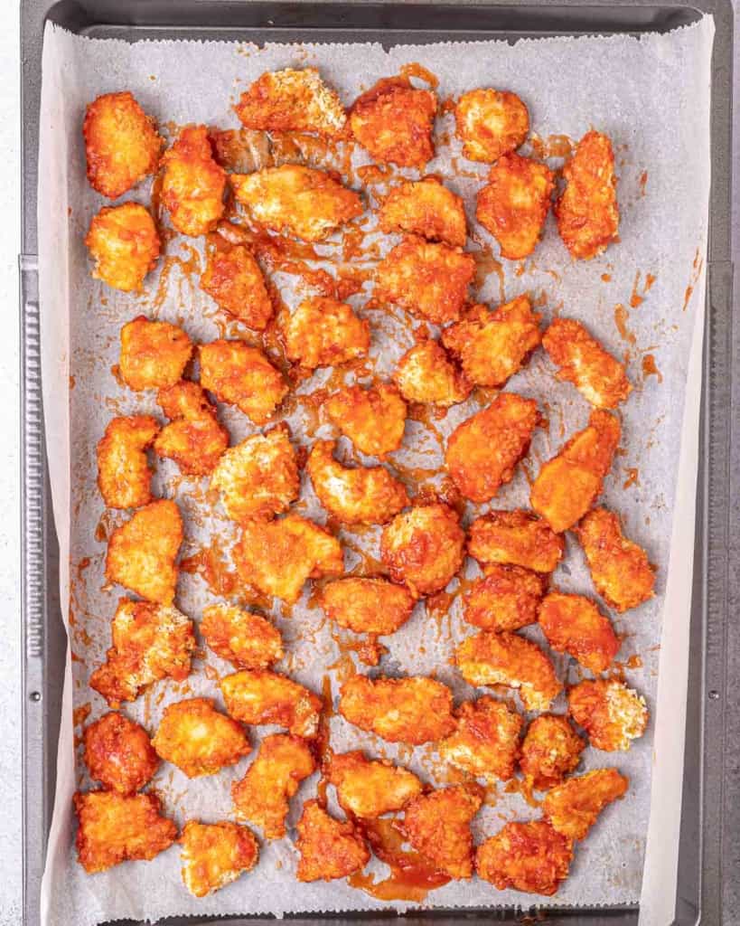 Sauce drizzled over chicken pieces on a baking sheet pan.