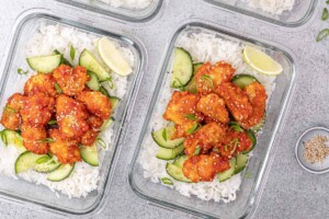 Meal prep bowls filled with honey sriracha chicken, rice and cucumbers.