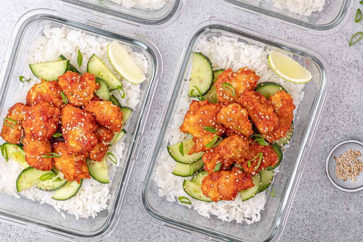 Meal prep bowls filled with honey sriracha chicken, rice and cucumbers.