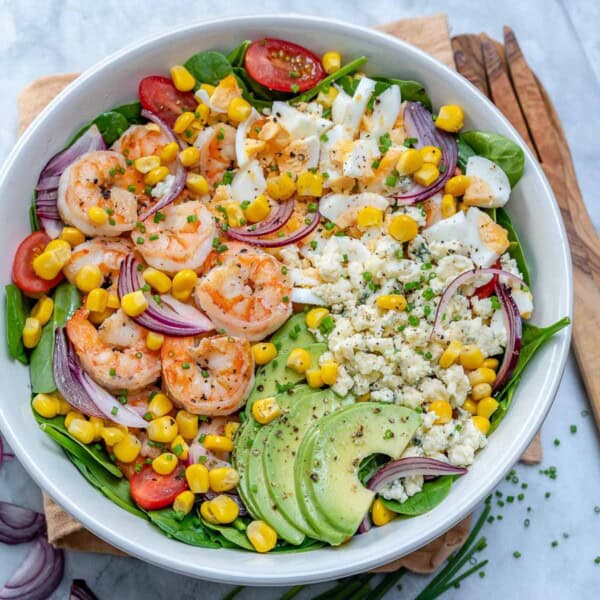 a round bowl of salad with shrimp avocado and corn.