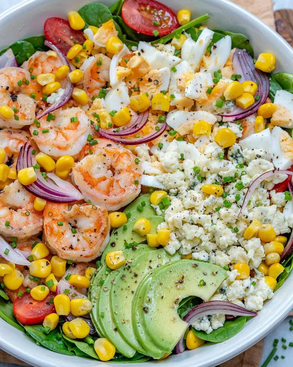 a bowl of salad topped with corn, tomatoes, seared shrimp, and sliced avocado.