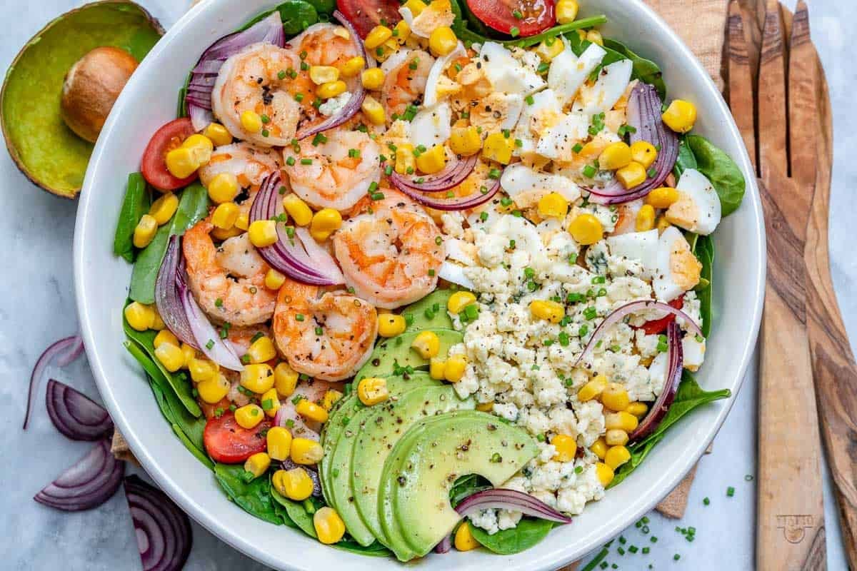 a bowl of salad topped with cooked shrimp and sliced avocado.
