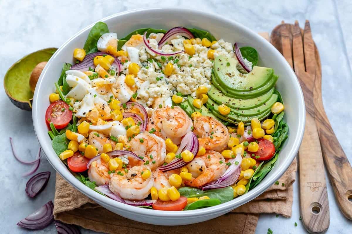 a round bowl filled with salad, topped with seared shrimp and corn.