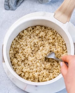 Cooked quinoa in a white pot being fluffed with a fork.