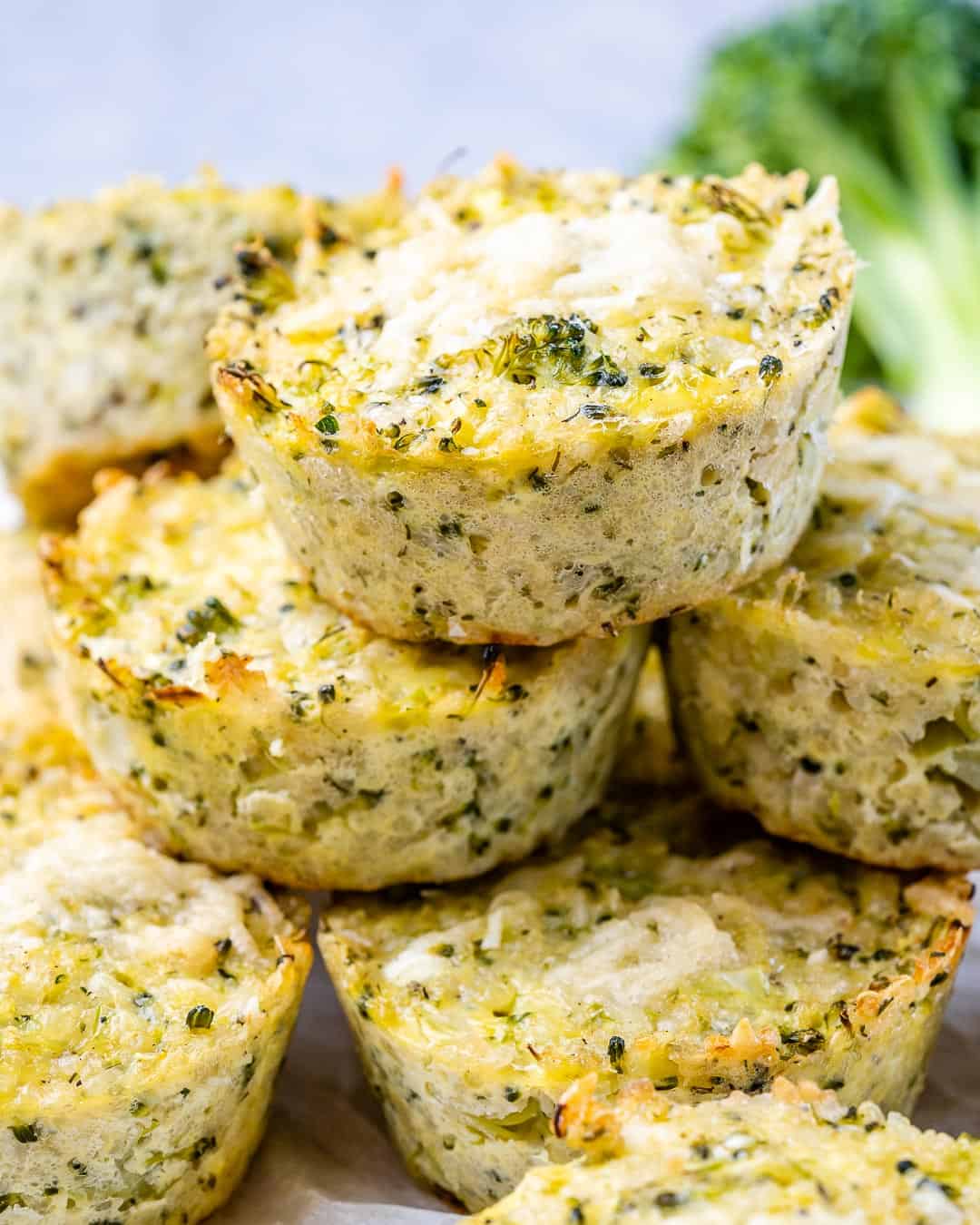 Pile of broccoli cheddar quinoa bites on a white surface with melted cheese visible on top.