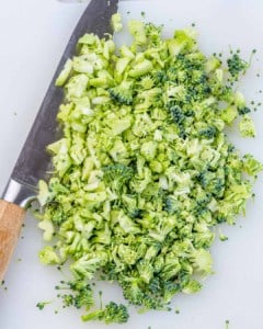 Finely chopped fresh broccoli on a cutting board with a knife nearby.