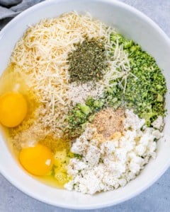 Mixing bowl filled with shredded cheddar cheese, eggs, chopped broccoli, and seasonings before combining.