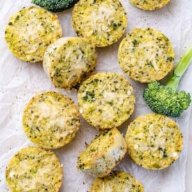 Overhead shot of several broccoli cheddar quinoa bites arranged on a white background next to some broccoli.