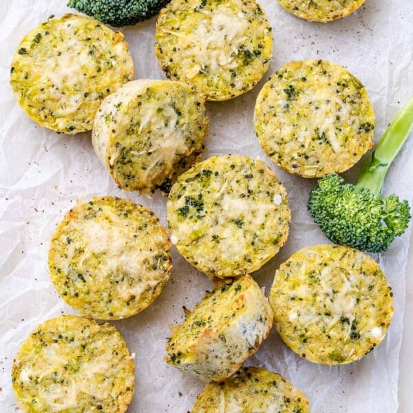 Overhead shot of several broccoli cheddar quinoa bites arranged on a white background next to some broccoli.