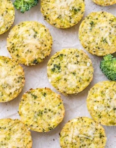 Freshly baked broccoli cheddar quinoa bites cooling on parchment paper, sprinkled with cheese.