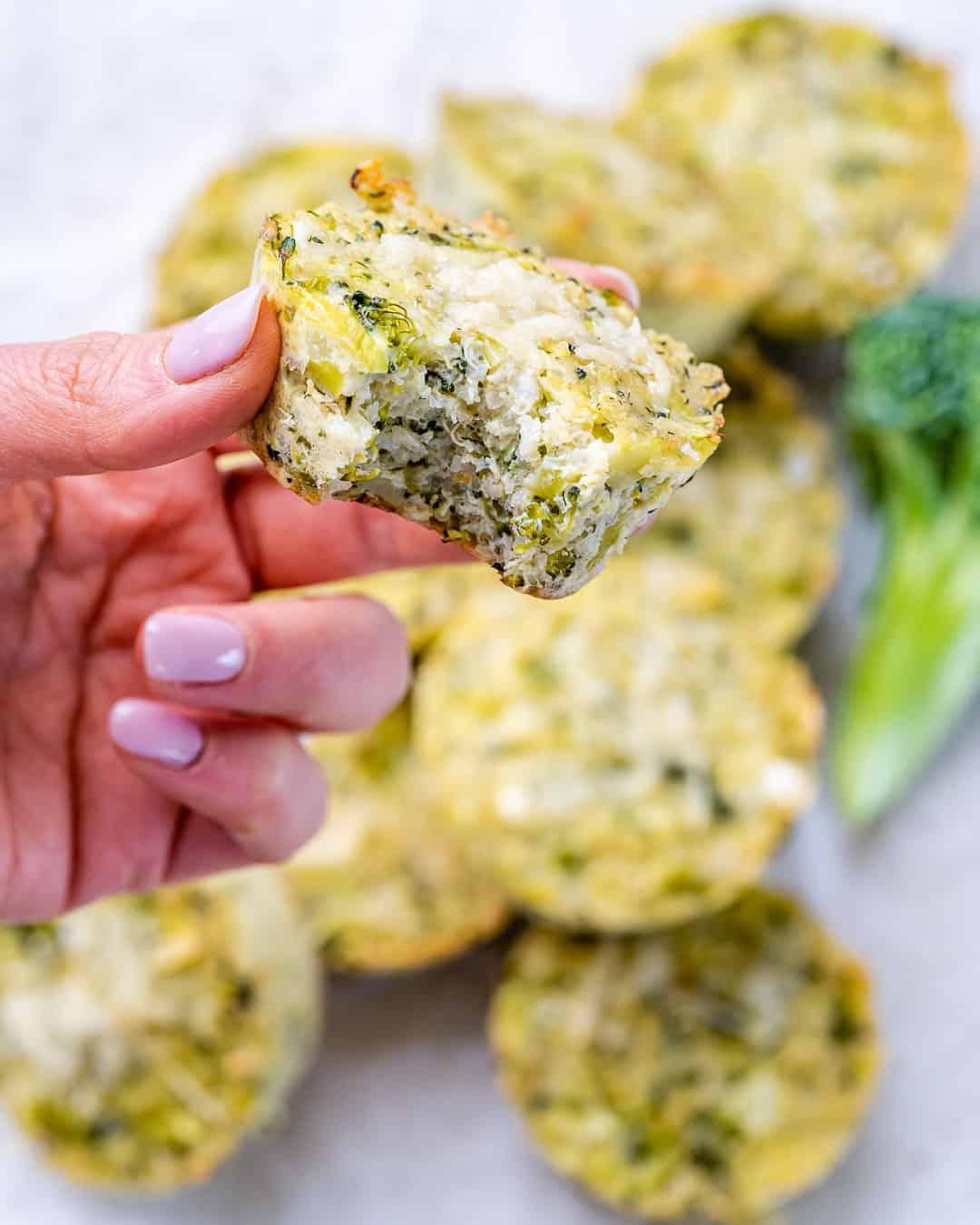 Close-up of a broccoli cheddar quinoa bite held between fingers, revealing cheesy, moist filling.
