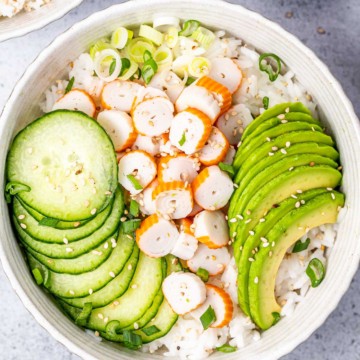 top view sushi bowl with crab meat, rice, sliced cucumber, avocado and sliced onions